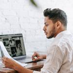 ethnic man reading document and working on laptop